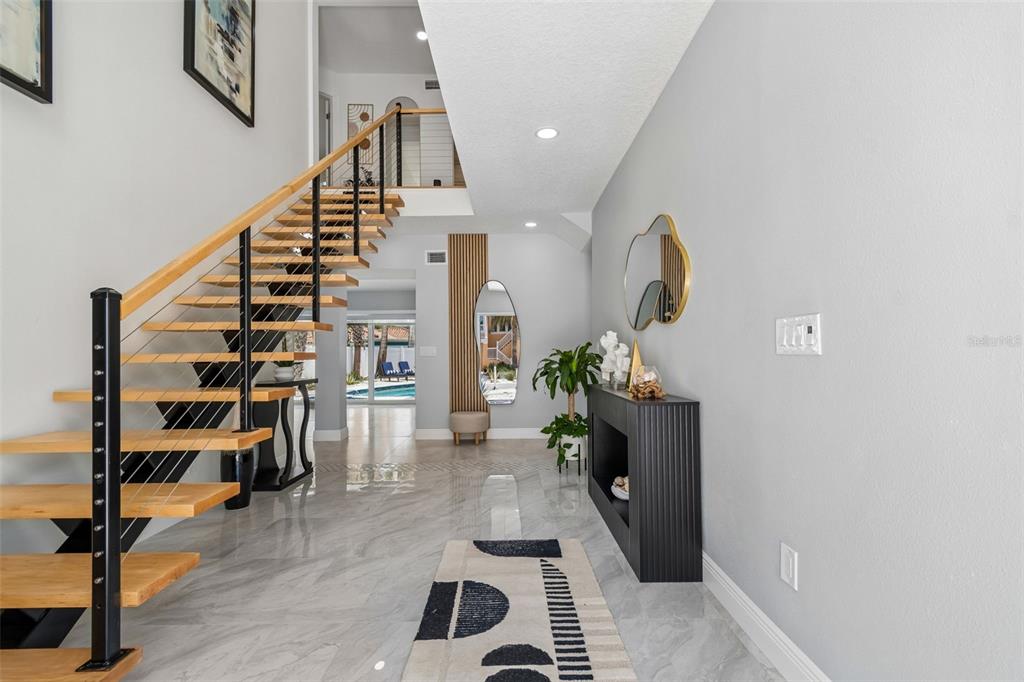 A modern entryway features a floating staircase, marble-look tile flooring, and a black console table — 933 ELDORADO AVENUE, CLEARWATER BEACH, FL