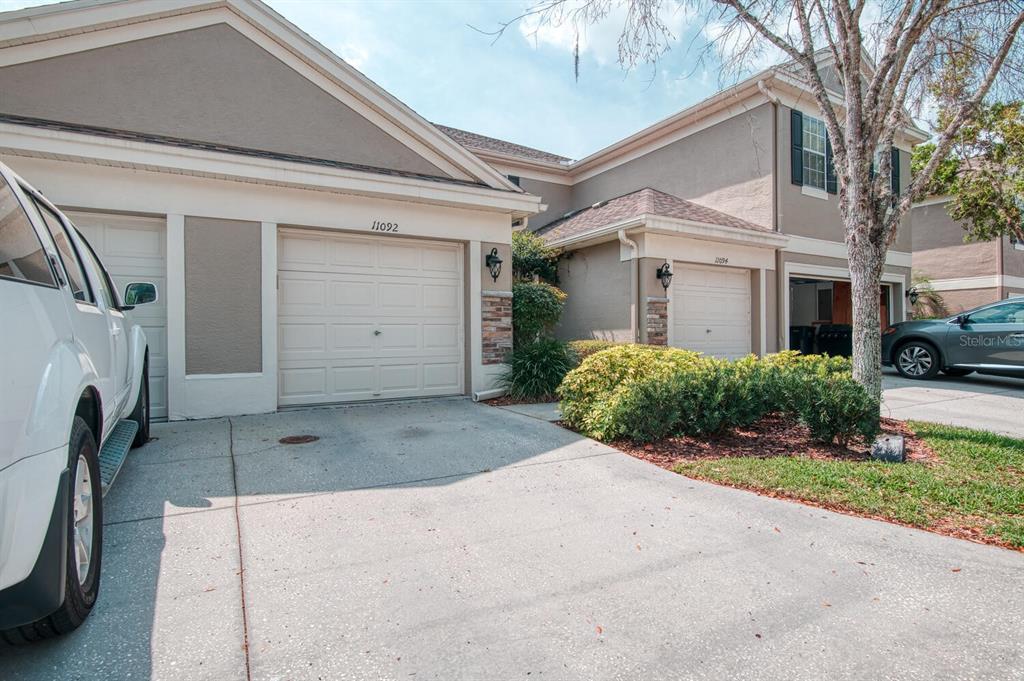 A view of two attached garage units with concrete driveways and a parked vehicle — 11092 WINDSOR PLACE CIRCLE, TAMPA, FL