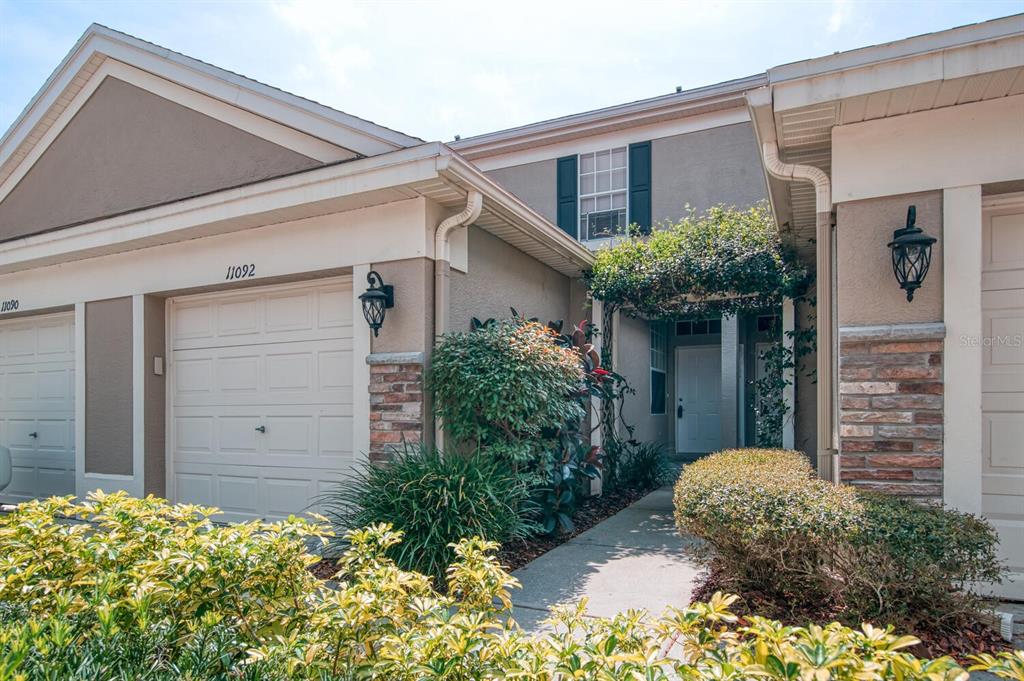 A two-story townhouse exterior features a garage, a covered entryway, and landscaped front bushes — 11092 WINDSOR PLACE CIRCLE, TAMPA, FL