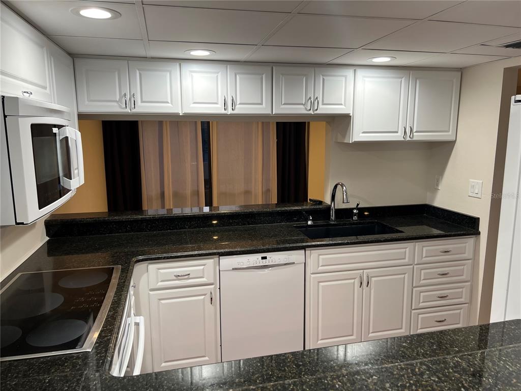 A kitchen features white cabinetry, dark granite countertops, a black sink, and a white dishwasher — 1210 CASEY KEY ROAD, NOKOMIS, FL