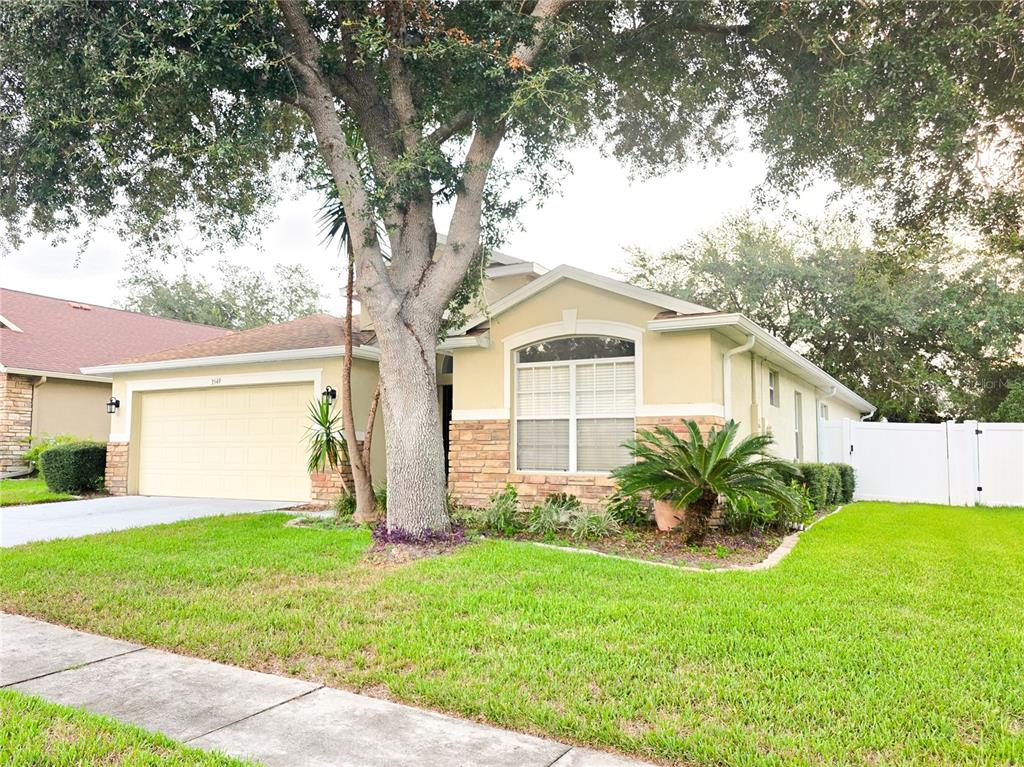 A single-story house with a beige exterior, stone accents, a two-car garage, and a large tree — 3549 BEAUMONT LOOP, SPRING HILL, FL