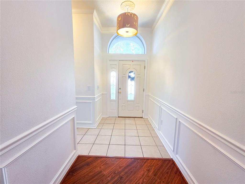 A foyer features white wainscoting, tile flooring, a wood-look transition, and a decorative pendant light — 3549 BEAUMONT LOOP, SPRING HILL, FL