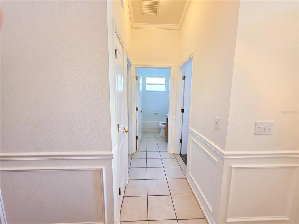 A hallway with tile flooring leads to a bathroom with a window and tub — 3549 BEAUMONT LOOP, SPRING HILL, FL