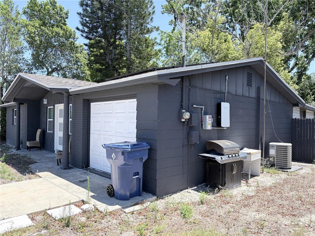 A dark gray house exterior features a white garage door, a Tesla Powerwall, and a grill — 3818 MOOG ROAD, HOLIDAY, FL