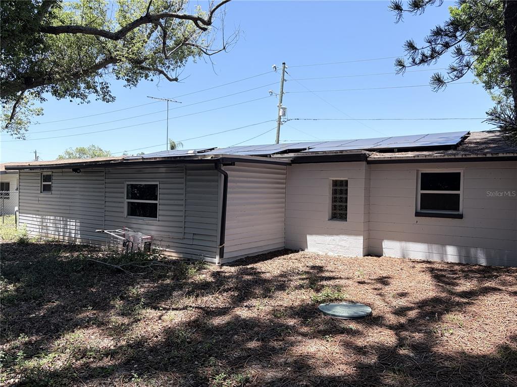 The exterior of a single-story house features white siding, solar panels, and a glass block window — 3818 MOOG ROAD, HOLIDAY, FL