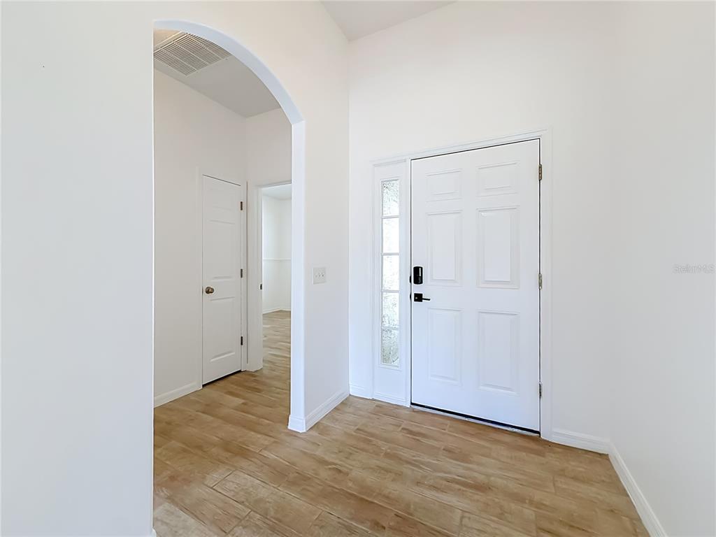 An entryway with white walls, wood-look tile flooring, an arched doorway, and a white front door — 240 JAMES CIRCLE, LAKE ALFRED, FL