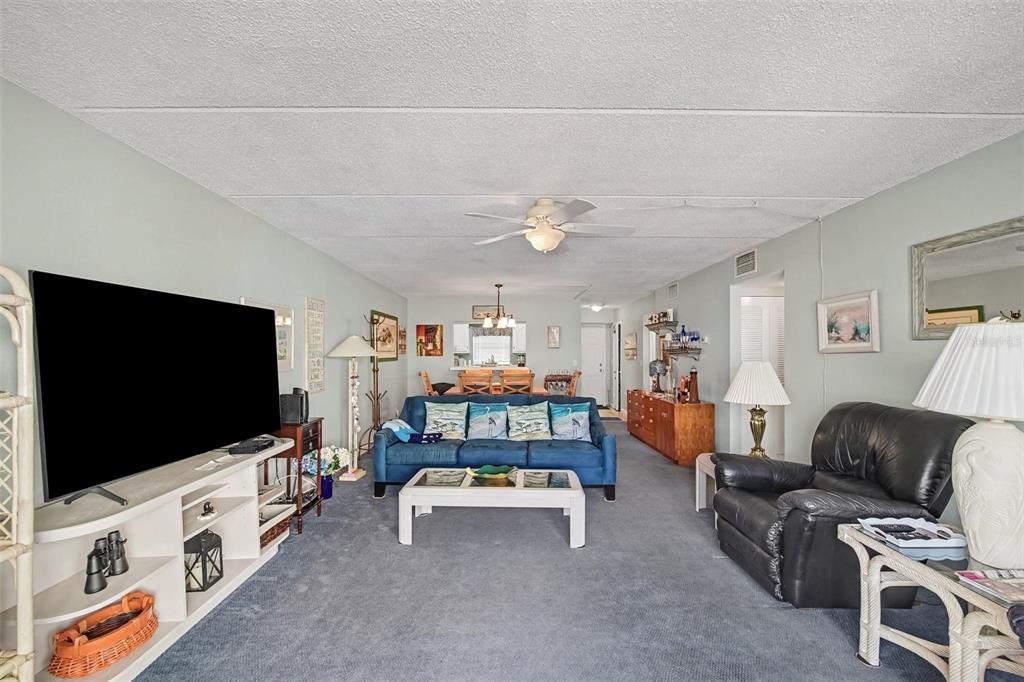A living room features a blue sofa, a large television, and a black leather armchair — 1926 OCEAN SHORE BOULEVARD UNIT 210, ORMOND BEACH, FL