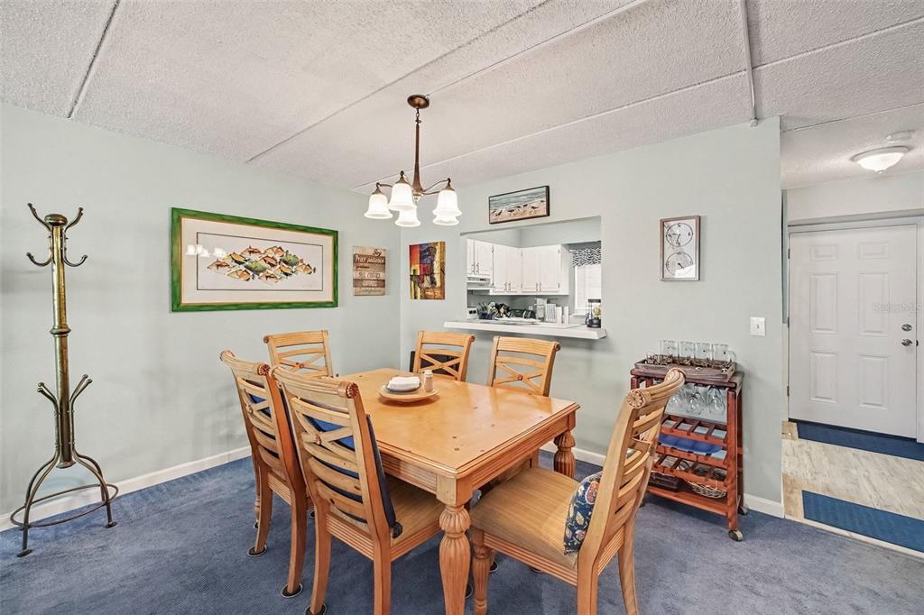 A dining area features a wooden table with chairs, a coat rack, and a kitchen pass-through — 1926 OCEAN SHORE BOULEVARD UNIT 210, ORMOND BEACH, FL