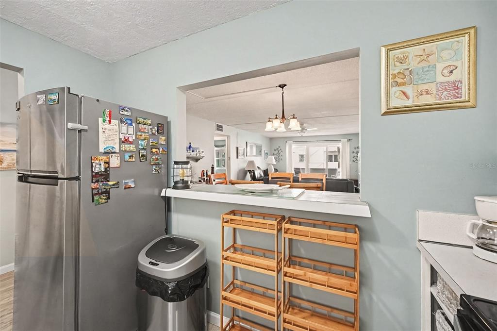 A kitchen with a stainless steel refrigerator, a pass-through window, and two wooden shelving units — 1926 OCEAN SHORE BOULEVARD UNIT 210, ORMOND BEACH, FL
