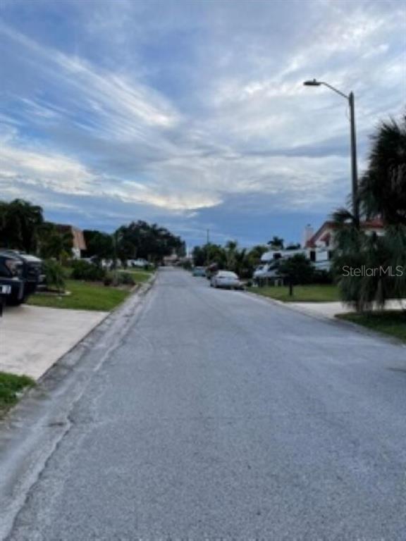 A paved residential street lined with houses, palm trees, and parked vehicles under a cloudy sky — 5008 ENSIGN LOOP, NEW PORT RICHEY, FL