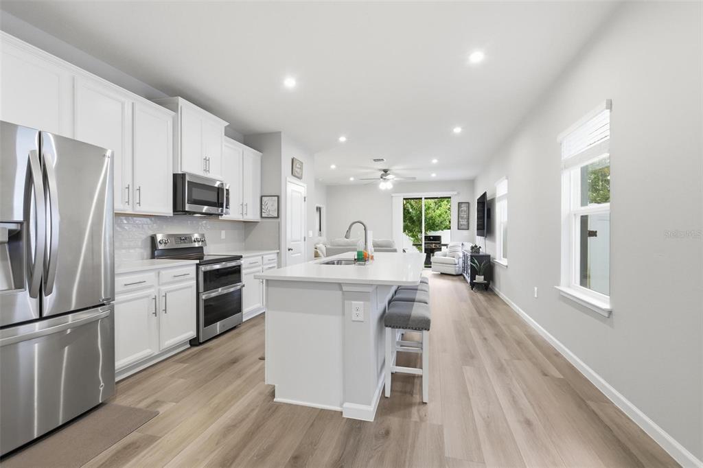 A modern kitchen features white cabinets, stainless steel appliances, a center island, and wood flooring — 7068 LANIER FALLS ROAD, DELAND, FL