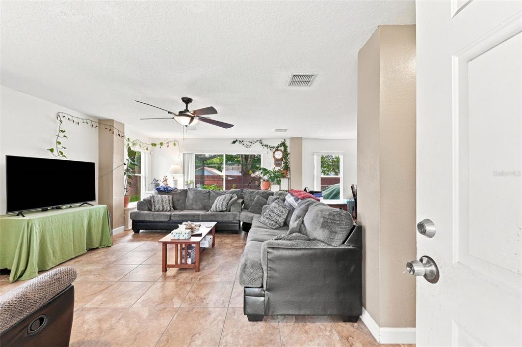 A living room features a large sectional sofa, a television on a green-covered stand, and tile flooring — 611 ABACO COURT, KISSIMMEE, FL
