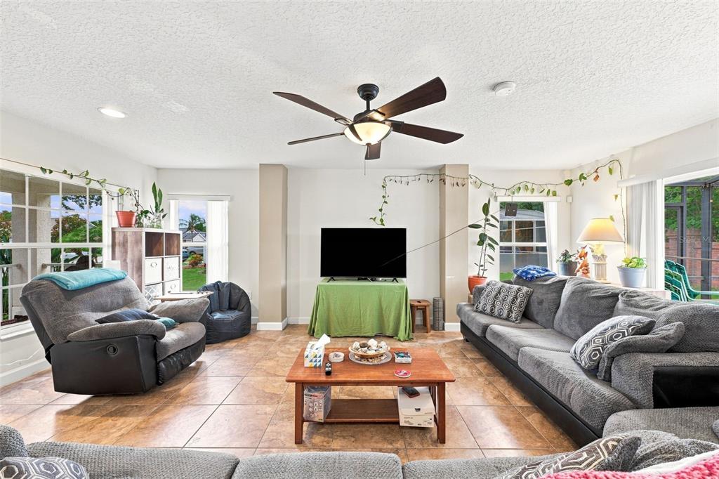 A living room features tile flooring, a ceiling fan, a television, and gray upholstered furniture — 611 ABACO COURT, KISSIMMEE, FL