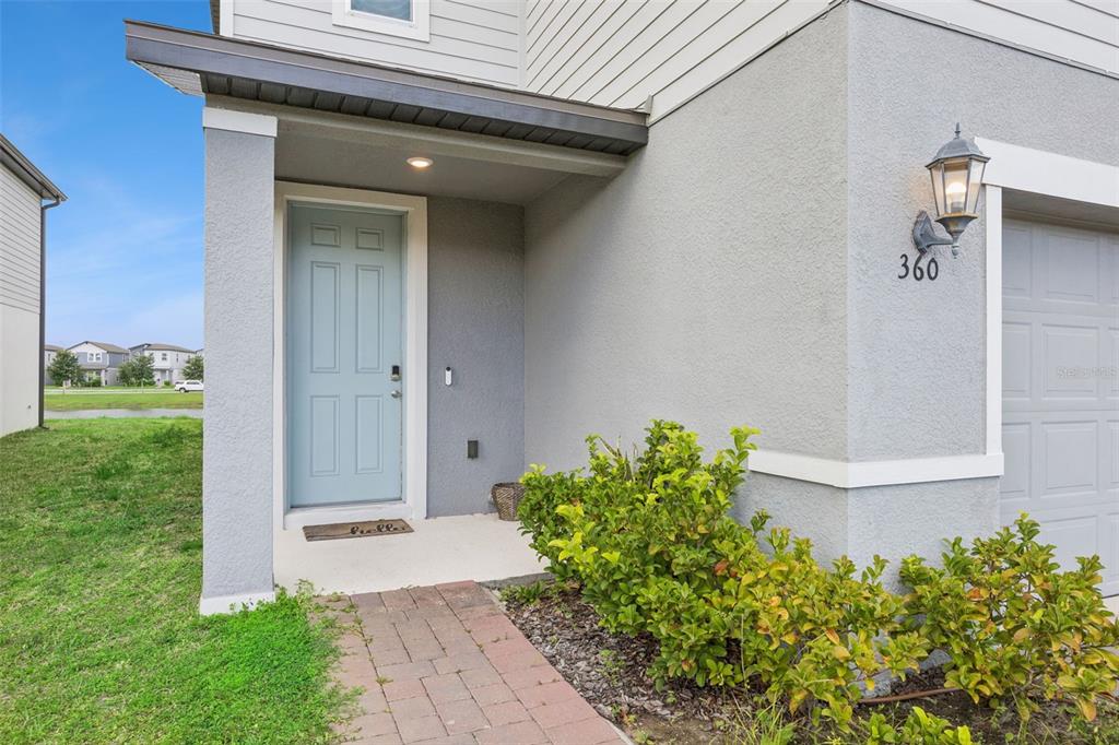 A light blue front door sits under a covered porch next to a gray garage — 360 WHISTLING DUCK TRAIL, ST CLOUD, FL