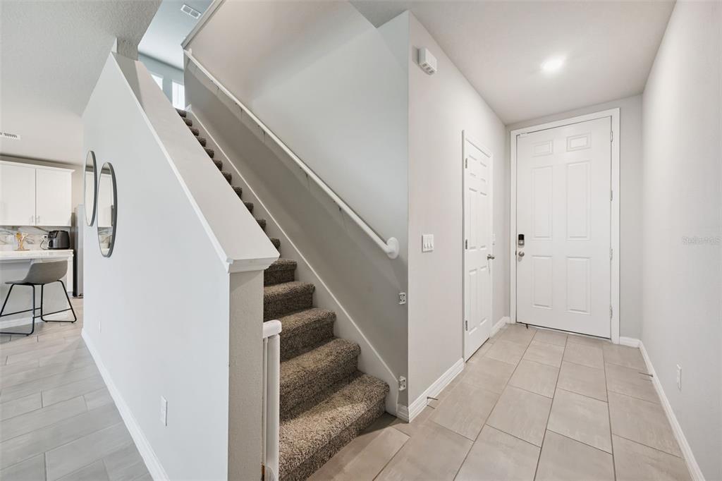 A carpeted staircase leads upstairs next to a tiled entryway with a white front door — 360 WHISTLING DUCK TRAIL, ST CLOUD, FL