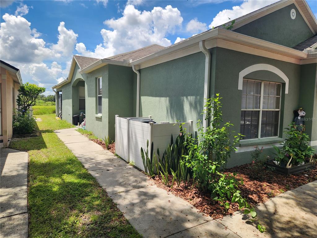 A side view of a green stucco house with a sidewalk and HVAC unit enclosure — 6210 KITERIDGE DRIVE, LITHIA, FL