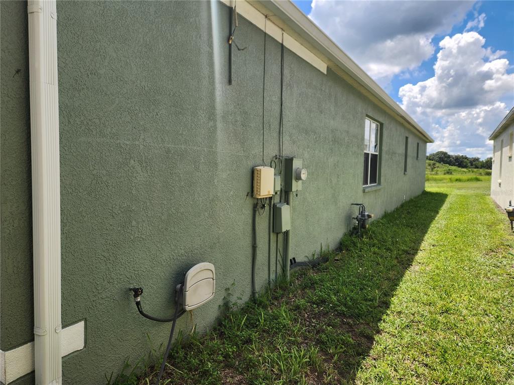 The exterior side wall of a house features utility meters, a window, and a downspout — 6210 KITERIDGE DRIVE, LITHIA, FL