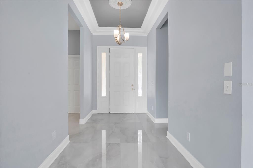A bright entryway features light gray walls, a tray ceiling, and polished marble-look tile flooring — 10842 WOODCHASE CIRCLE, ORLANDO, FL