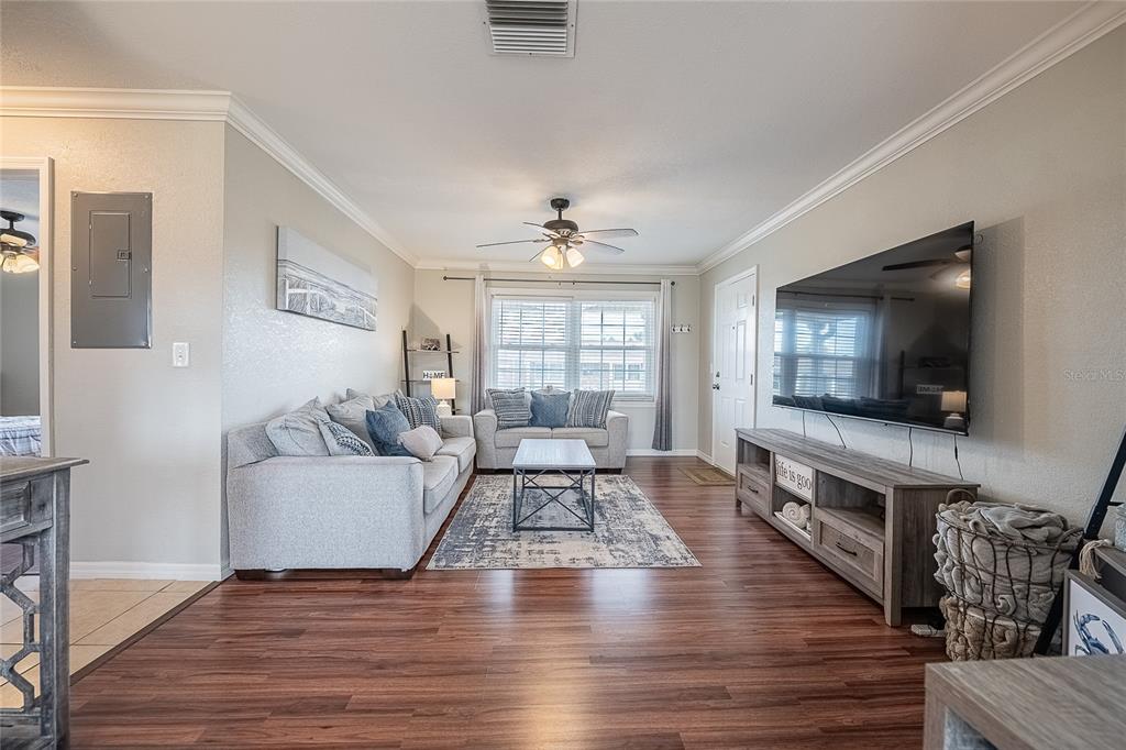 A living room features wood-look flooring, a gray sofa, a television, and a ceiling fan — 1920 E EDGEWOOD DRIVE UNIT L4, LAKELAND, FL