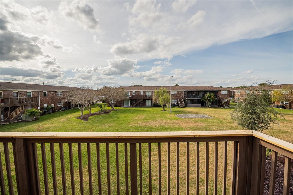 A view from a wooden balcony overlooking a grassy courtyard between brick apartment buildings — 1920 E EDGEWOOD DRIVE UNIT L4, LAKELAND, FL