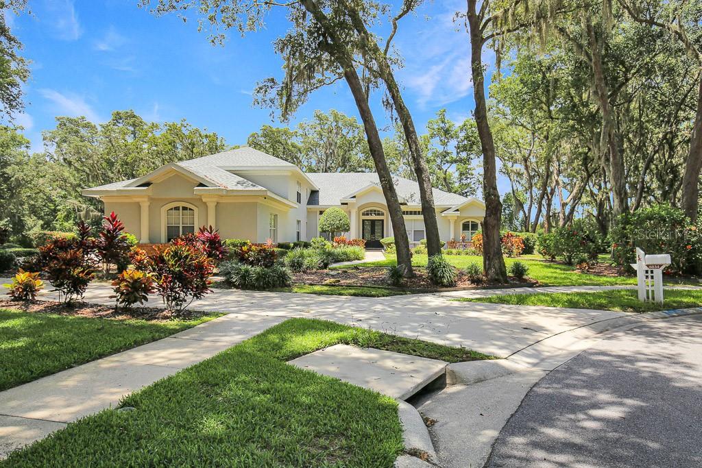 A single-story house with a light-colored exterior, a circular driveway, and mature trees — 6034 HAMMOCK HILL AVENUE, LITHIA, FL
