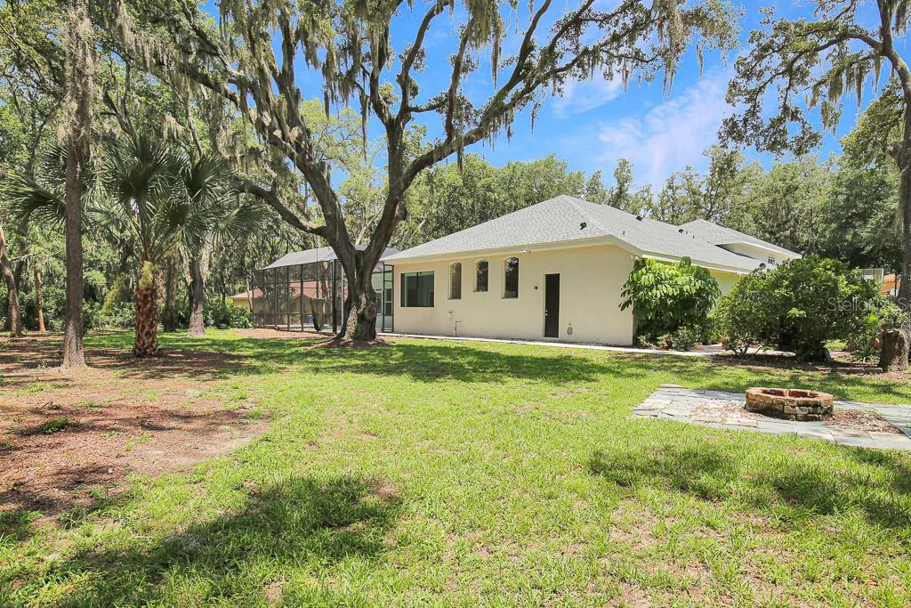 A backyard with a fire pit, a screened-in patio, and large oak trees behind a house — 6034 HAMMOCK HILL AVENUE, LITHIA, FL