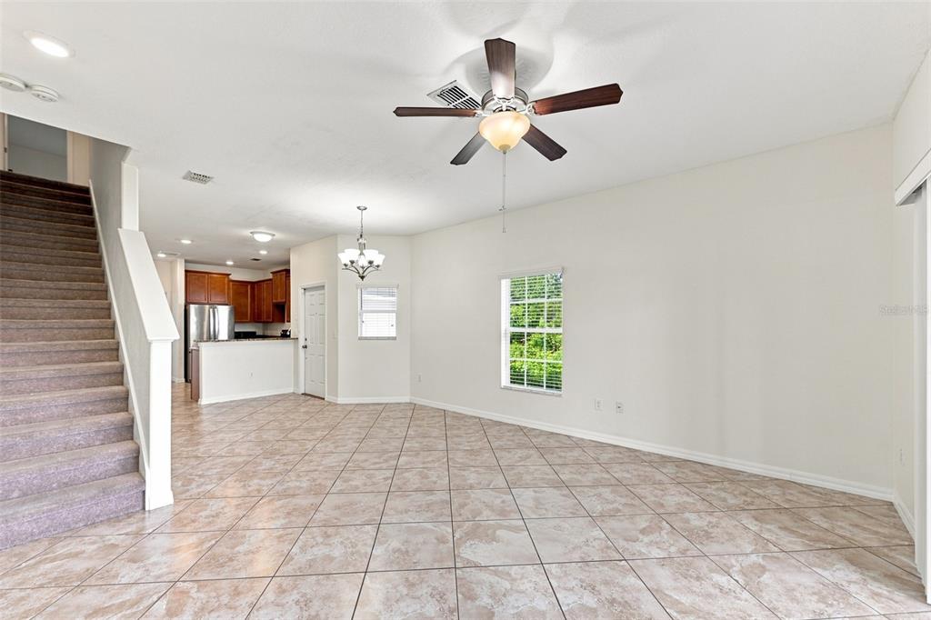An open-concept living and dining area features tile flooring, a ceiling fan, and a staircase — 31141 CLARIDGE PLACE, WESLEY CHAPEL, FL