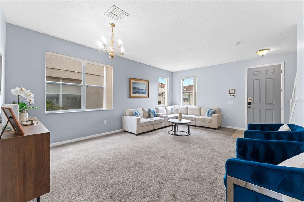A living room features light blue walls, beige carpet, a sectional sofa, and blue armchairs — 213 WILLOW VIEW DRIVE, DAVENPORT, FL