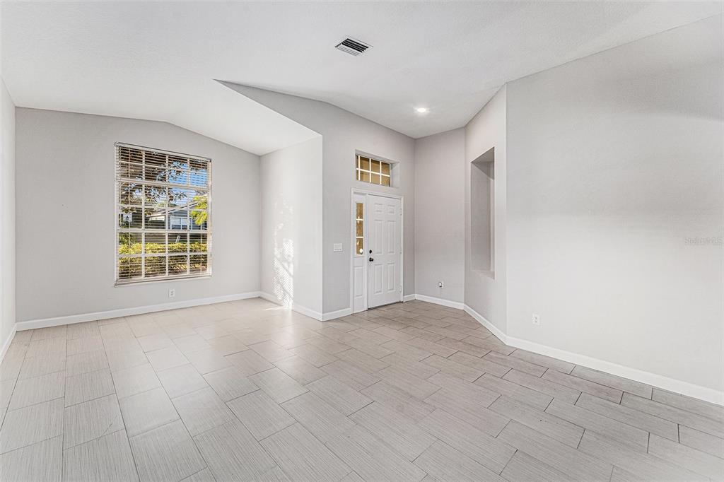 An empty room with light gray tile flooring, vaulted ceilings, and a white front door — 3316 STONEBRIDGE TRAIL, VALRICO, FL