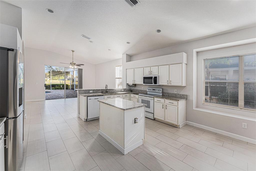 A kitchen features white cabinets, granite countertops, a center island, and light-colored tile flooring — 3316 STONEBRIDGE TRAIL, VALRICO, FL