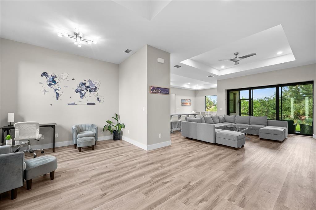 A spacious living room features light wood flooring, a large gray sectional, and a wall map — 15761 AQUA CIRCLE, PORT CHARLOTTE, FL