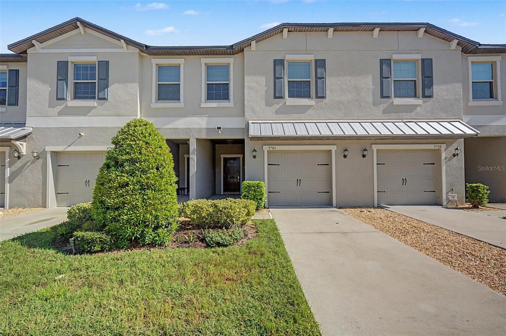 The exterior of a townhouse features a covered entryway, a garage, and a metal awning — 9706 PEMBROOKE PINES DRIVE, SUN CITY CENTER, FL