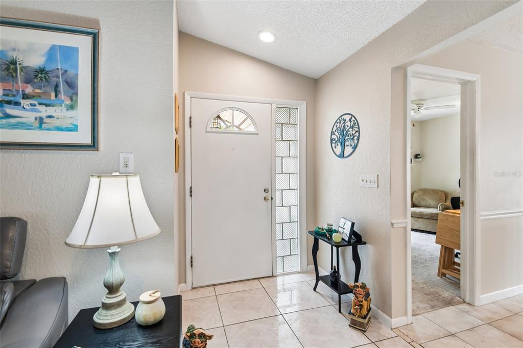 An entryway features a white front door with a glass sidelight, tile flooring, and vaulted ceilings — 12596 93RD WAY, LARGO, FL