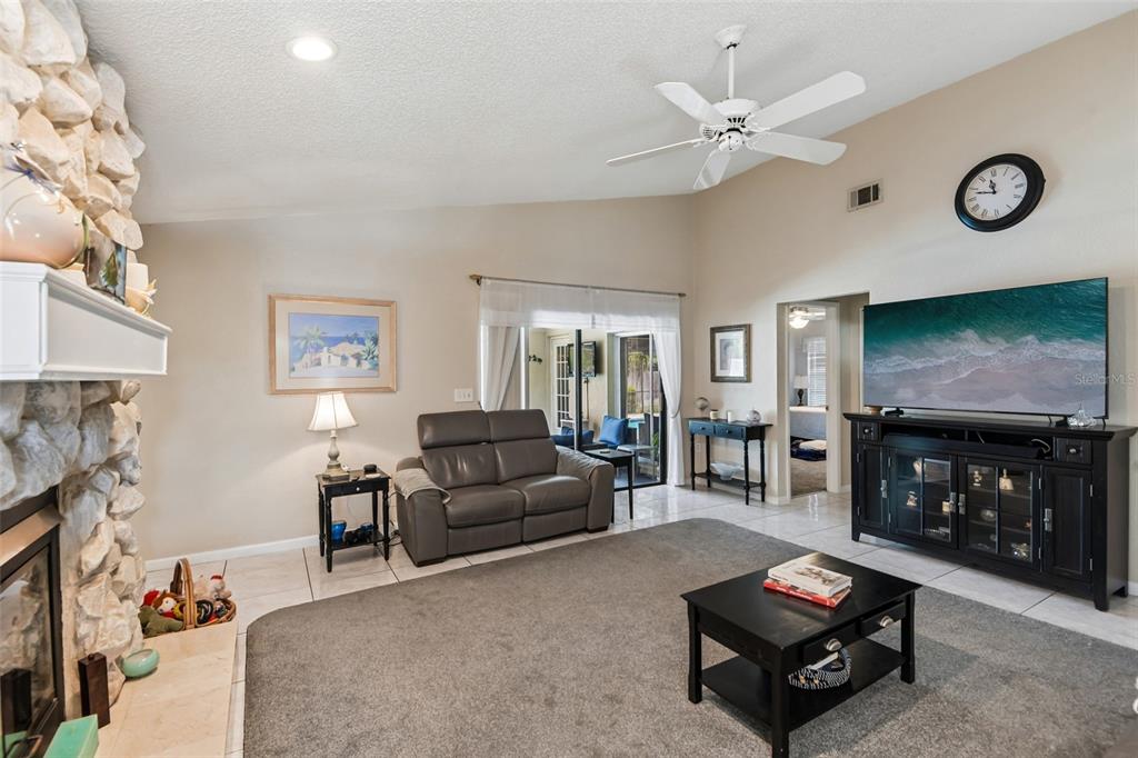 A living room features a stone fireplace, gray sofa, black media console, and ceiling fan — 12596 93RD WAY, LARGO, FL