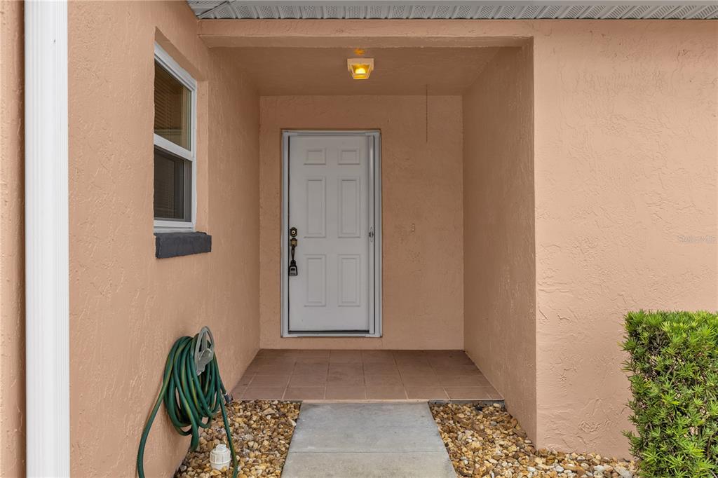 A white front door is centered in a recessed, peach-colored stucco entryway with tiled flooring — 805 SAN CARLOS COURT, LADY LAKE, FL