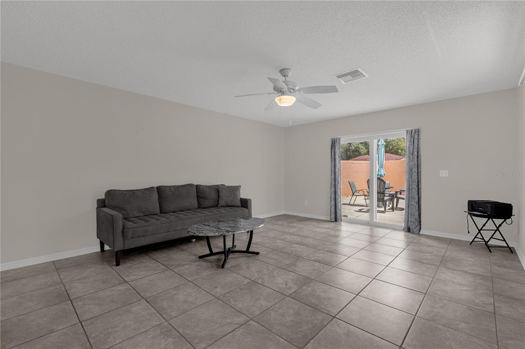 A living room with gray tile flooring, a dark sofa, a coffee table, and sliding doors — 805 SAN CARLOS COURT, LADY LAKE, FL
