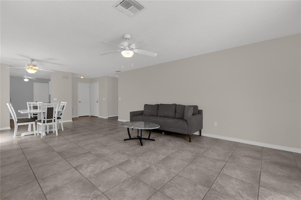 A living room with gray tile flooring, a dark sofa, and an adjacent dining area — 805 SAN CARLOS COURT, LADY LAKE, FL