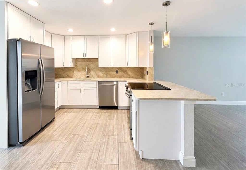 A modern kitchen features white cabinets, stainless steel appliances, and a peninsula with a cooktop — 681 PALM VIEW DRIVE UNIT C1, NAPLES, FL