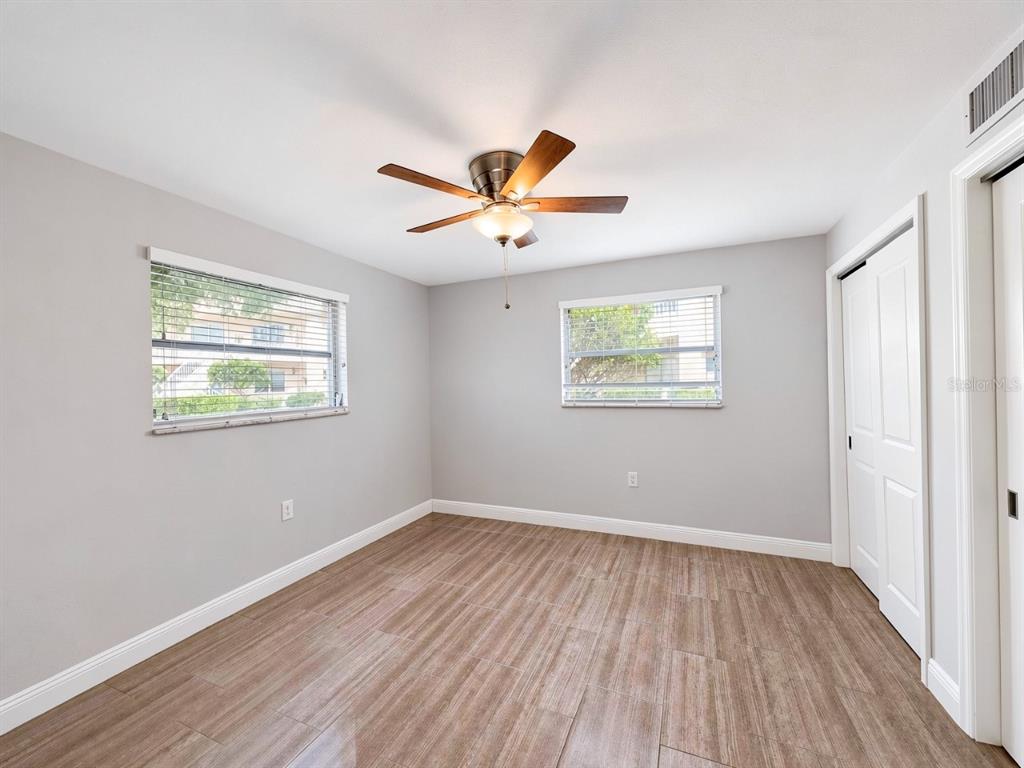 An empty bedroom with gray walls, wood-look tile flooring, a ceiling fan, and two windows — 681 PALM VIEW DRIVE UNIT C1, NAPLES, FL