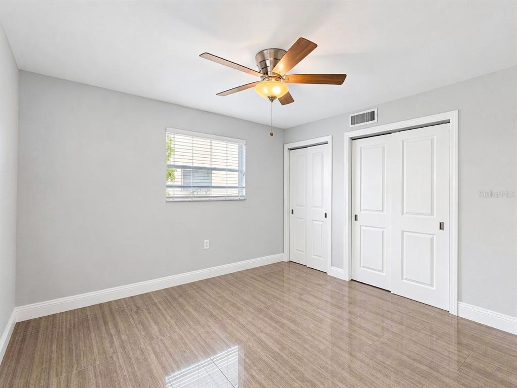 A bedroom with light gray walls, wood-look tile flooring, a ceiling fan, and two closets — 681 PALM VIEW DRIVE UNIT C1, NAPLES, FL