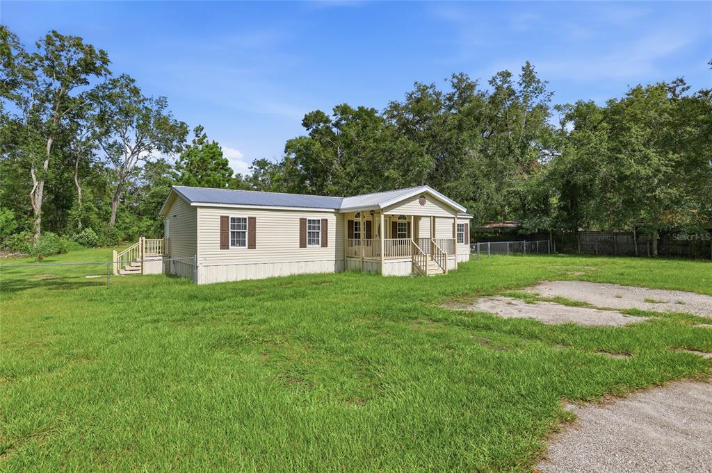 A beige manufactured home with a front porch sits on a grassy lot with trees — 9528 NW 235TH TERRACE, ALACHUA, FL