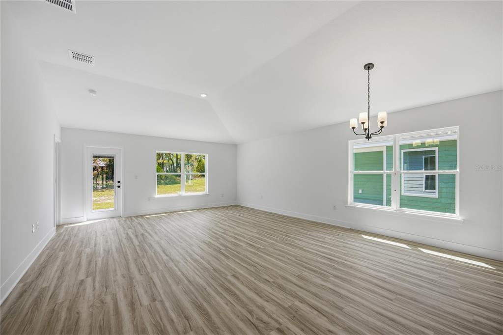 A bright, empty room features light wood-look flooring, white walls, a vaulted ceiling, and windows — 2618 SW 250TH TERRACE, NEWBERRY, FL