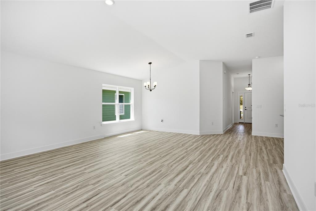 An empty room with light wood-look flooring, white walls, a chandelier, and a window — 2618 SW 250TH TERRACE, NEWBERRY, FL