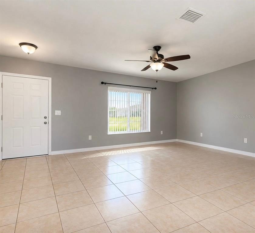 A living room with gray walls, tile flooring, a ceiling fan, and a white door — 61 WALNUT DRIVE, OCALA, FL