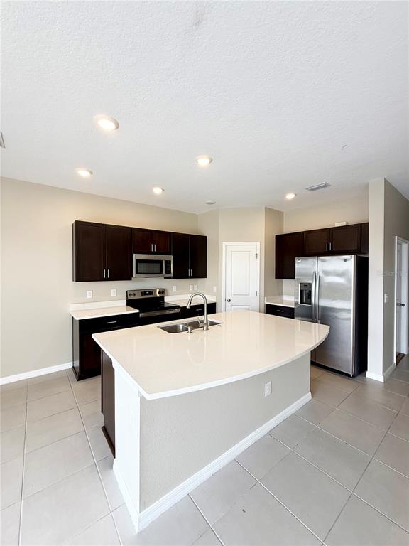 A kitchen features dark wood cabinets, stainless steel appliances, and a large white quartz island — 2309 ALEE LANE, WESLEY CHAPEL, FL