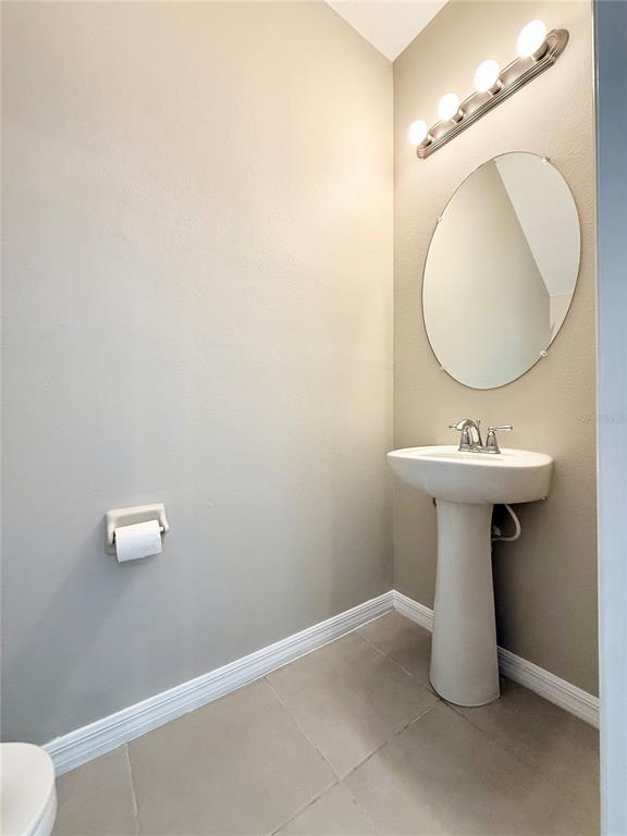 A half bathroom features a pedestal sink, oval mirror, wall lighting, and tile flooring — 2309 ALEE LANE, WESLEY CHAPEL, FL