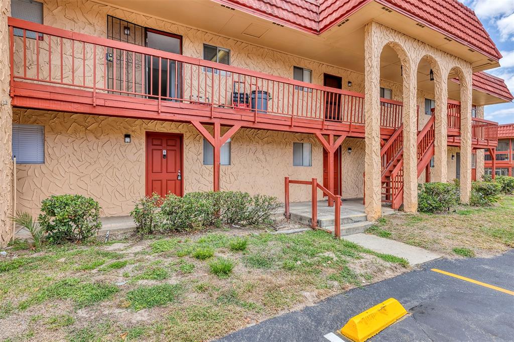 A two-story apartment building exterior features a red wooden balcony, arched pillars, and stucco walls — 2864 N POWERS DRIVE UNIT 150, ORLANDO, FL
