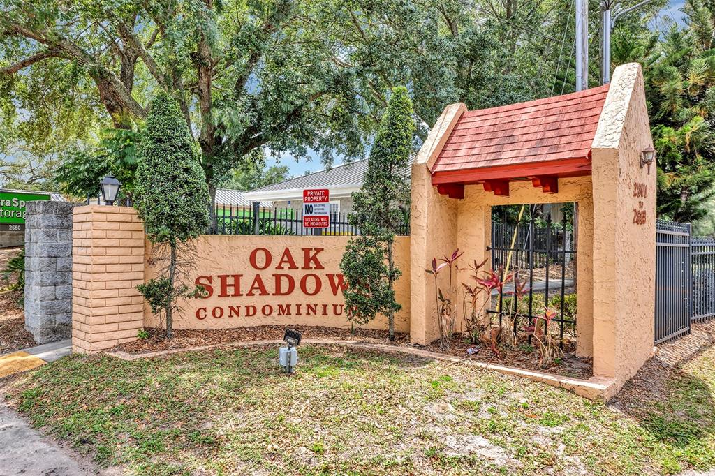 The entrance sign for Oak Shadow Condominiums features a stucco wall with a red roof — 2864 N POWERS DRIVE UNIT 150, ORLANDO, FL