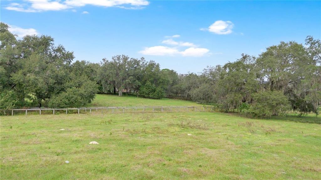 A grassy field is enclosed by a wooden fence with mature trees in the background — MICRO RACETRACK ROAD, FRUITLAND PARK, FL