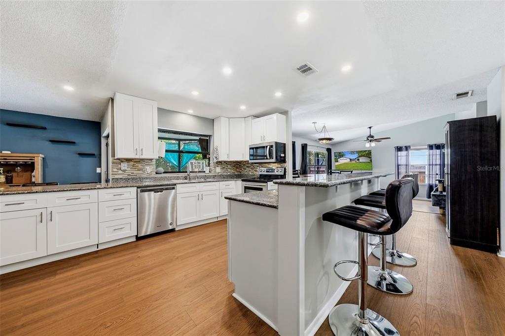 A kitchen features white cabinets, granite countertops, stainless steel appliances, and a breakfast bar — 3916 BLOOMING HILL LANE, PALM HARBOR, FL